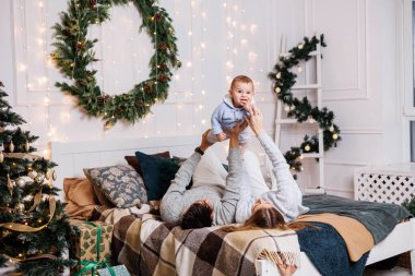 Küçük bir oğlu olan neşeli genç bir çift Noel ağacının yanındaki yatakta oynuyorlar. Yeni yıl içleri yatak odasında. Oyuncaklı Noel ağacı. Şenlikli aile ortamı.