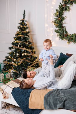 Küçük bir oğlu olan neşeli genç bir çift Noel ağacının yanındaki yatakta oynuyorlar. Yeni yıl içleri yatak odasında. Oyuncaklı Noel ağacı. Şenlikli aile ortamı.