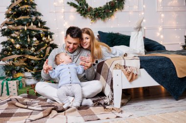 Noel ağacının yanında mutlu bir ailesi olan tatlı bir çocuk. Süslü bir Noel ağacının yakınındaki yatak odasında küçük bir çocuklu bir aile. Şenlikli yeni yıl atmosferi. Aile kutlaması