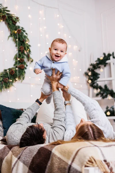 stock image A cheerful young couple with a little son are playing on the bed near the Christmas tree. New Year's interior in the bedroom. Christmas tree with toys. Festive family atmosphere.