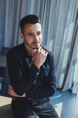 Gözlüklü ve siyah tişörtlü genç başarılı erkek işçi masamızda oturmuş, modern ofiste dizüstü bilgisayarla ekrana bakarak proje üzerinde çalışıyor.