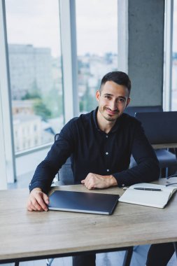 Beyaz gömlekli başarılı bir iş adamı modern bir ofiste dizüstü bilgisayar kullanarak bir masada oturuyor. Ofiste çalışma ortamı.