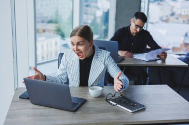 Bir bayan yönetici, modern bir ofisteki dizüstü bilgisayarını bir meslektaşının arka planına karşı kullanarak masada oturuyor. Ofiste çalışma ortamı.