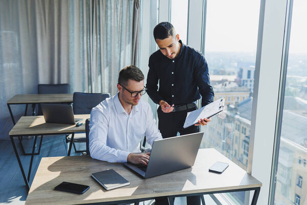 Two business men are creating a project while looking at the laptop screen during a meeting in a modern boardroom. Work process in a modern office