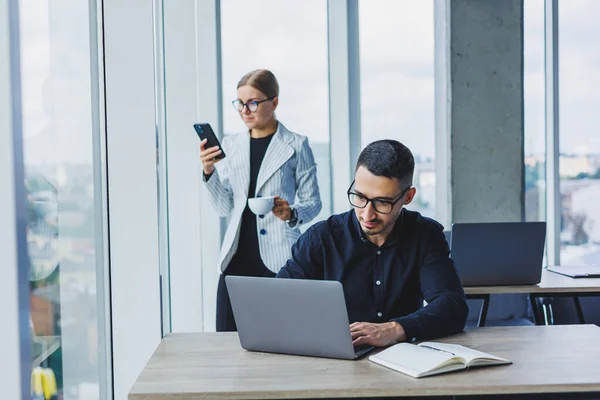 Stock image A businessman is working on a laptop while talking while his colleague is listening. Work in a modern bright office