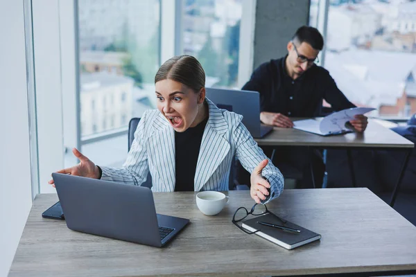 在一个现代化的办公室里 一位女经理在一位同事的背景下 使用笔记本电脑坐在办公桌前 办公室的工作气氛 — 图库照片