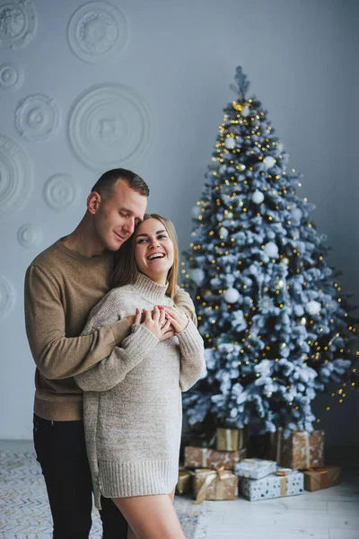 stock image A happy couple in love are standing near the Christmas tree and hugging. New Year's atmosphere. Tender hugs near the Christmas tree of two people