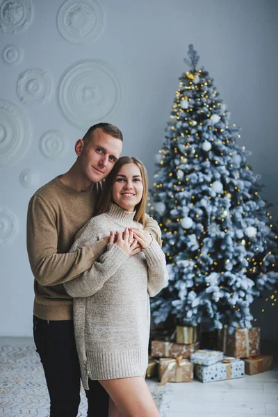 A happy couple in love are standing near the Christmas tree and hugging. New Year\'s atmosphere. Tender hugs near the Christmas tree of two people