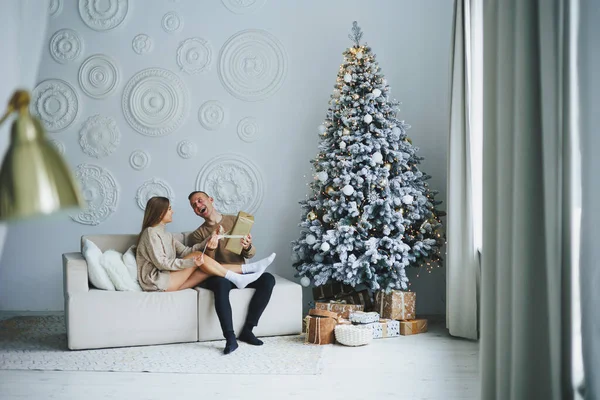 A couple in love on New Year\'s Eve in a cozy home environment near the Christmas tree. New Year\'s love story. Beautiful couple in sweaters posing in studio. A guy and a girl celebrate the new year