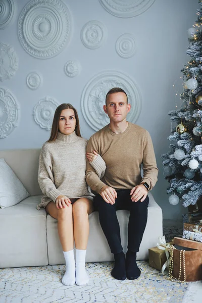 A couple in love on New Year\'s Eve in a cozy home environment near the Christmas tree. New Year\'s love story. Beautiful couple in sweaters posing in studio. A guy and a girl celebrate the new year