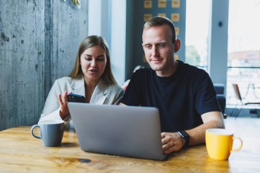İki erkek ve kadın meslektaşı laptopta iş tartışıyorlar, çalışma alanında birlikte oturuyorlar ve konuşuyorlar, genç erkek ve bayan öğrenciler birlikte çalışıyorlar.