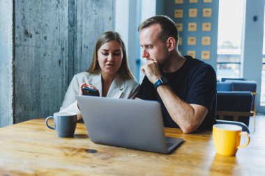 İki erkek ve kadın meslektaşı laptopta iş tartışıyorlar, çalışma alanında birlikte oturuyorlar ve konuşuyorlar, genç erkek ve bayan öğrenciler birlikte çalışıyorlar.