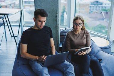 Öğrenciler pencerenin yanındaki çalışma alanında oturuyor ve bir dizüstü bilgisayar projesinde birlikte çalışıyorlar. Neşeli iş arkadaşları yöneticiler birlikte dizüstü bilgisayara bakar ve gülümserler..