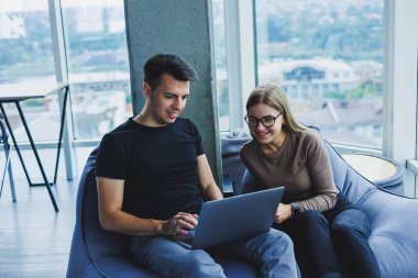 Öğrenciler pencerenin yanındaki çalışma alanında oturuyor ve bir dizüstü bilgisayar projesinde birlikte çalışıyorlar. Neşeli iş arkadaşları yöneticiler birlikte dizüstü bilgisayara bakar ve gülümserler..