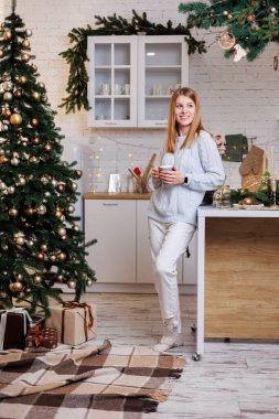 Gülümseyen genç bir kadın bir Noel ağacının yanında oturuyor. Evde Noel 'in rahat atmosferi.