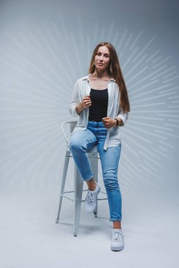 Beyaz tişörtlü, siyah tişörtlü ve arka planda kot pantolonlu gülümseyen genç bir kadın. Yüzünde gülümseme olan esmer bir kadının portresi.