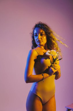 Sadece bej bir elbise giyen kıvırcık, hayalperest genç kadın beyaz arka planda duruyor. Kadın bej iç çamaşırı.