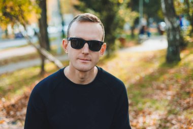 Parktaki bankta oturan, güneş gözlüklü yakışıklı, başarılı genç adam.