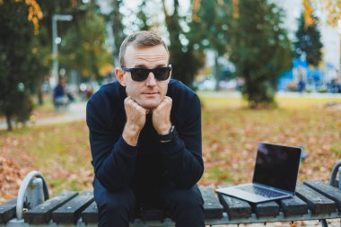 Parktaki bankta oturan, güneş gözlüklü yakışıklı, başarılı genç adam.