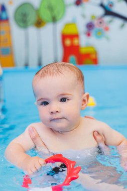 Küçük bir çocuk bebek havuzunda yüzmeyi öğreniyor. Çocuk gelişimi. Çocuklar için ilk yüzme dersleri