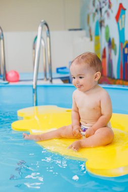 Çocuklar için yüzme dersleri. Küçük bir çocuk bebek havuzunda yüzmeyi öğreniyor. Çocuk gelişimi. Çocuklar için ilk yüzme dersleri