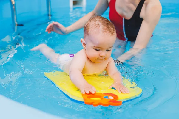 A beautiful mother teaches teaches her little son how to swim in the pool. A child is having fun in the water with his mother. Child development. First swimming lessons for children