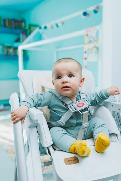 Küçük yakışıklı bir çocuk beslenmek için yüksek bir sandalyede oturuyor. Yemek için çocuk mutfak sandalyesi. Çocuk mobilyası.