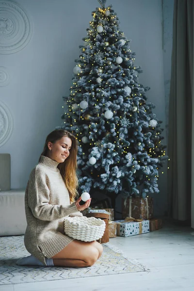 一位身穿针织毛衣 脸上挂着笑容的金发年轻女子站在一棵装饰过的圣诞树旁 新年庆祝活动 — 图库照片