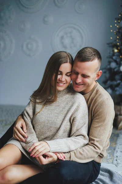 A couple in love rejoices on New Year\'s Eve in a cozy home environment. New Year\'s love story. A beautiful couple in sweaters and Christmas trees. A guy and a girl celebrate the new year