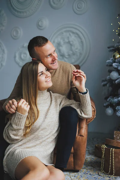 A couple in love rejoices on New Year's Eve in a cozy home environment. New Year's love story. A beautiful couple in sweaters and Christmas trees. A guy and a girl celebrate the new year