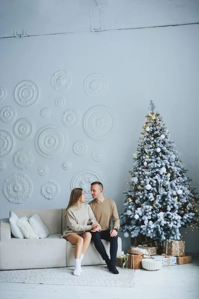 A couple in love rejoices on New Year\'s Eve in a cozy home environment. New Year\'s love story. A beautiful couple in sweaters and Christmas trees. A guy and a girl celebrate the new year