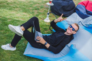 Şirin bir genç adam sokakta yumuşak bir sandalyeye oturur ve dizüstü bilgisayarda çalışır, rahatlar ve nargile içer. Uzak çalışma