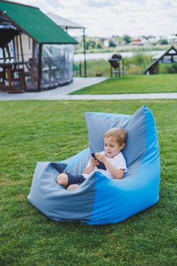 Güneşli bir günde küçük bir çocuk dışarıda oturuyor ve telefonda oyun oynuyor..