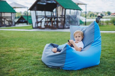Güneşli bir günde küçük bir çocuk dışarıda oturuyor ve telefonda oyun oynuyor..
