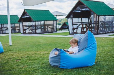 Güneşli bir günde küçük bir çocuk dışarıda oturuyor ve telefonda oyun oynuyor..