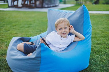 Güneşli bir günde küçük bir çocuk dışarıda oturuyor ve telefonda oyun oynuyor..