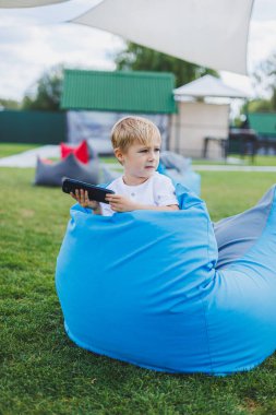 Aleti olan modern bir çocuk. Güneşli bir günde küçük bir çocuk dışarıda oturuyor ve telefonda oyun oynuyor..