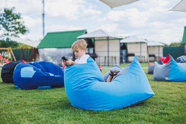 Aleti olan modern bir çocuk. Güneşli bir günde küçük bir çocuk dışarıda oturuyor ve telefonda oyun oynuyor..