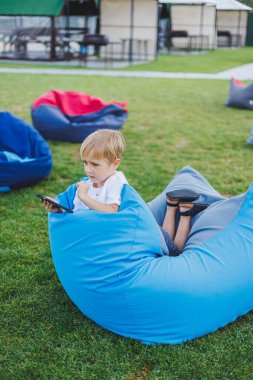 Aleti olan modern bir çocuk. Güneşli bir günde küçük bir çocuk dışarıda oturuyor ve telefonda oyun oynuyor..