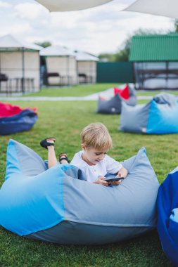 Aleti olan modern bir çocuk. Güneşli bir günde küçük bir çocuk dışarıda oturuyor ve telefonda oyun oynuyor..