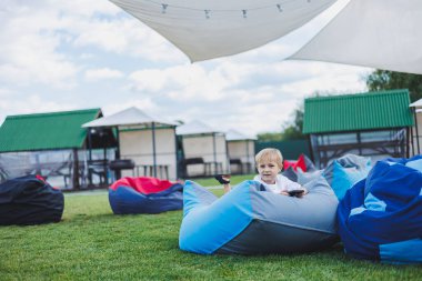 Aleti olan modern bir çocuk. Güneşli bir günde küçük bir çocuk dışarıda oturuyor ve telefonda oyun oynuyor..