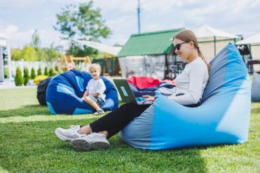 Genç bir kadın parkta yumuşak bir sandalyeye oturur ve dizüstü bilgisayarla çalışır. Dışarıda çalış.