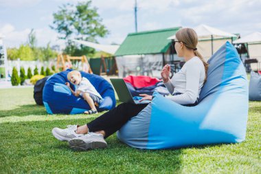 Genç bir kadın parkta yumuşak bir sandalyeye oturur ve dizüstü bilgisayarla çalışır. Dışarıda çalış.