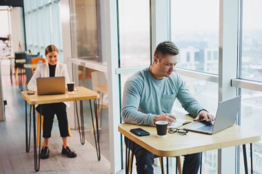 Genç bir erkek yönetici büyük pencereli bir ofiste oturuyor ve bir dizüstü bilgisayarda çalışıyor. Yakışıklı bir işadamı bir kafede ödevini yapıyor..