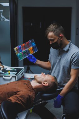 Dişlerin ortodontik tedavisi. Dişçiyle randevusu olan genç bir adam. Doktor hastanın dişlerine metal diş telleri takıyor. Ağız bakımı. Seçici odak