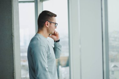 Günlük kıyafetlerle başarılı bir adam çalışma odasının penceresinde dikiliyor ve telefonla konuşuyor. Genç bir yönetici uzaktan çalışıyor..