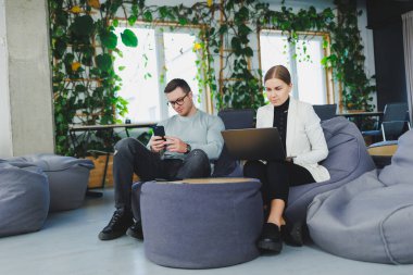 Bir adam ve bir kadın dinlenme odasında oturuyorlar ve farklı aletler kullanıyorlar. Tatmin oldular ve uzaktan çalışıyorlar..