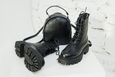 Kadınların siyah deri çizmeleri ve beyaz arka planda siyah deri bir sırt çantası var. Kadın modası