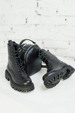 Kadınların siyah deri çizmeleri ve beyaz arka planda siyah deri bir sırt çantası var. Kadın modası