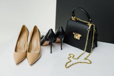 Topuklu şık kadın ayakkabıları beyaz arka planda siyah bir el çantasının yanında duruyor. Yazmak için yer